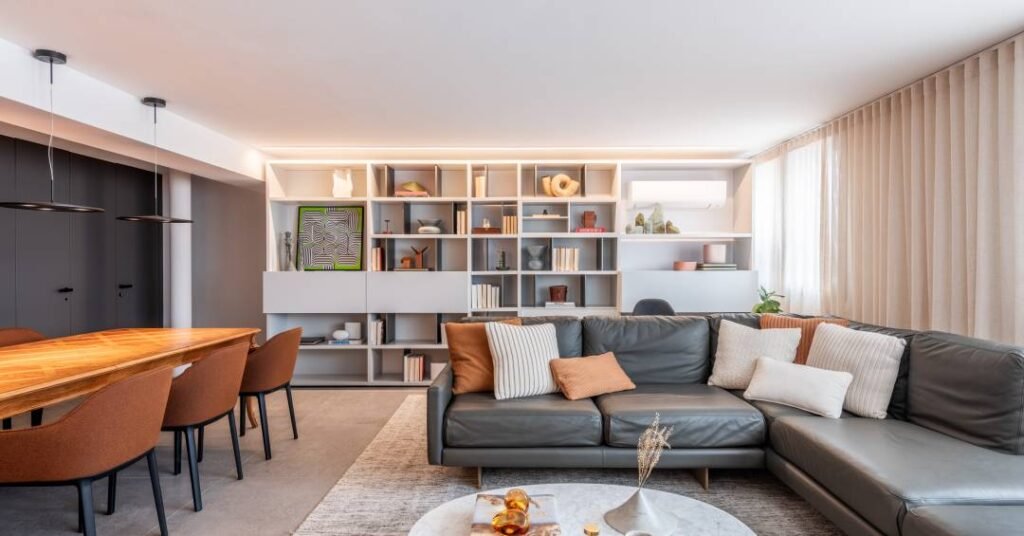 Apartamento tem marcenaria cinza clara na cozinha e na estante de nichos na sala