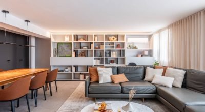 Apartamento tem marcenaria cinza clara na cozinha e na estante de nichos na sala