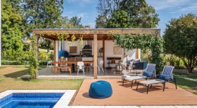 Charmosa área gourmet de casa tem pergolado florido, forno de pizza azul e piso em cerâmica